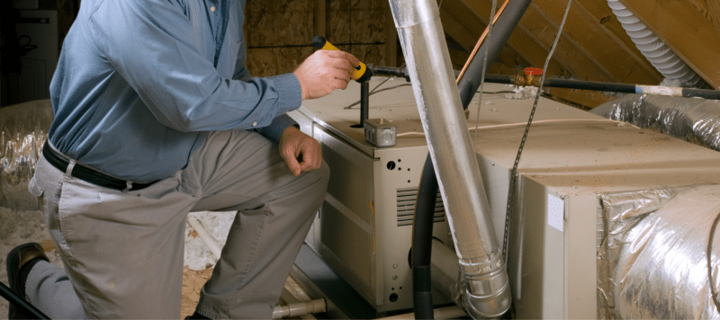 technician using a flashlight to inspect a furnace